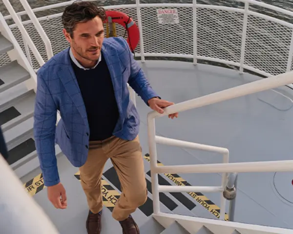 Man dressed in a blazer, sweater, and khaki pants on a boat