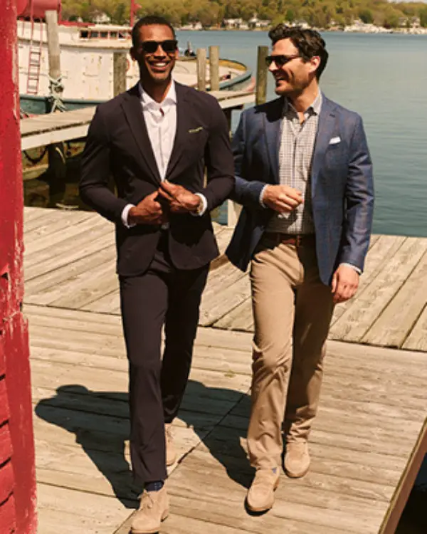 Two men dressed in blazers and nice pans walking down a dock.
